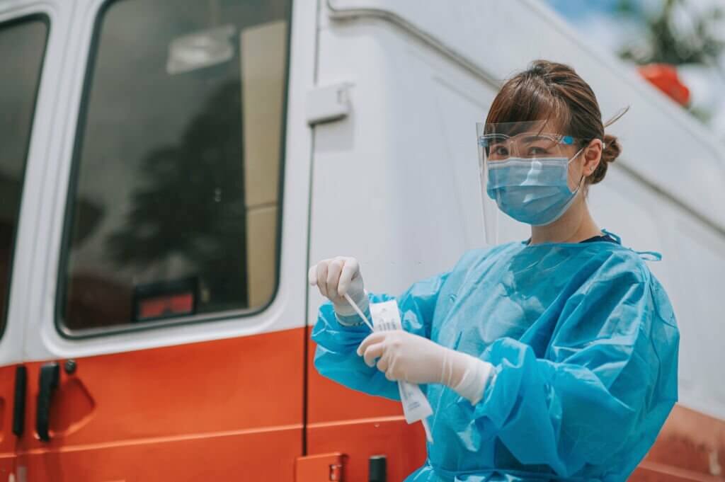 救护车旁的室外亚裔华人女医生带着个人防护设备，准备从病人身上取鼻咽拭子
